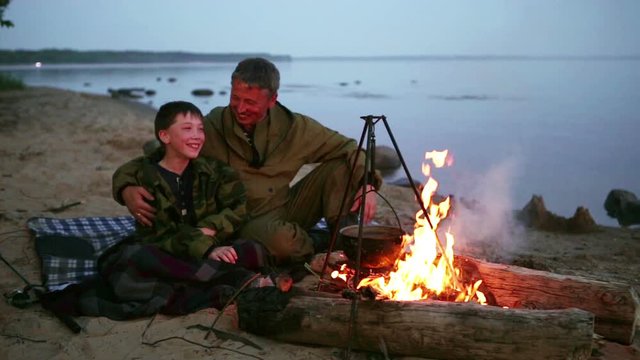 Father and son sitting around the campfire at the lake.