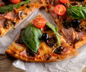A slice of pizza with bacon, tomatoes and basil on a wooden tabl