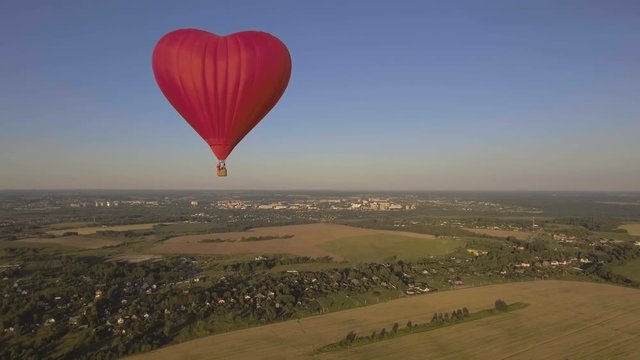 Red balloon in the shape of a wheat heart.Aerial view:Hot air balloon in the sky over a field in the countryside in the beautiful sky and sunset.Aerostat fly in the countryside. 4K video,ultra HD.