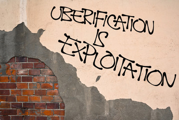 Uberification Is Exploitation - Handwritten graffiti sprayed on the wall, anarchist aesthetics -...