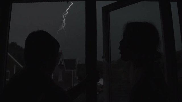 Children looking out of a dark bedroom window waiting for lightning to strike from a large thunderstorm 