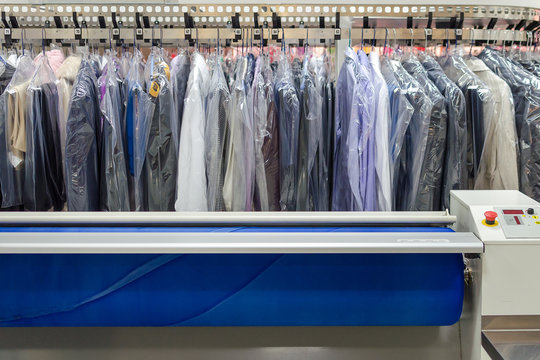 Clean clothes on hangers in the laundry room with industrial cylinder heated drying ironer
