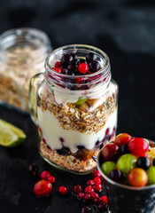 Muesli, fresh berries and yogurt in glass mason jar on wooden ta
