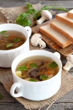 Homemade mushroom soup in a bowl, bread slices on a chopping board, fresh mushrooms and green parsley on a wooden table. Dietary soup with champignons and vegetables. Rustic style