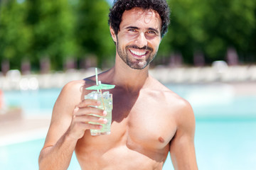 Handsome young man drinking a cocktail while relaxing in a swimming pool