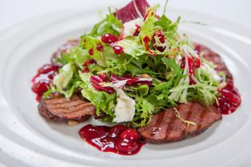 Salad with veal grilled, fresh lettuce and arugula, sweet and sour cherry sauce on white round plate