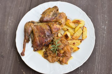 Roasted or baked Guinea fowl served with baked potatoes and sweet onion with apples and raisins. Meal spiced by rosemary and black pepper is served on the white plate and old rustic wooden table.