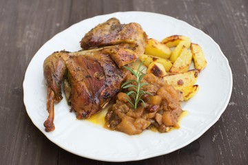 Roasted or baked Guinea fowl served with baked potatoes and sweet onion with apples and raisins. Meal spiced by rosemary and black pepper is served on the white plate and old rustic wooden table.