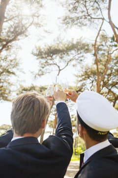 Male graduates toasting champagne flutes at university park