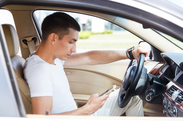 Stylish young brunette man uses the phone in the car