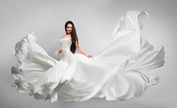 beautiful young girl in flying white dress. Flowing fabric. Light white cloth flying in the wind