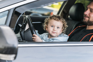 Little girl sitting in the car, on the lap of his father