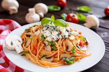 Spaghetti pasta salad with tomato sauce, fried mushrooms, blue cheese and basil on a wooden background
