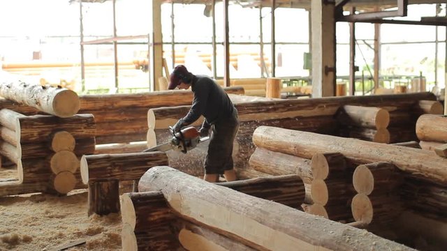 Man cuts off beam chainsaw for future home. Construction works with a wooden structure