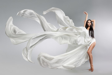 Fototapeta na wymiar beautiful young girl in flying white dress. Flowing fabric. Light white cloth flying in the wind