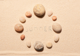 Round frame of sea stones with summer lettering drawn on sand