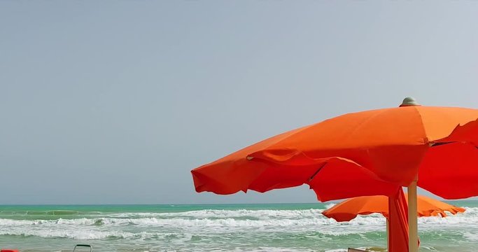 Orange beach umbrellas flapping in the wind, with sea waves in background, slow motion