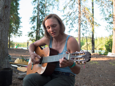 Young woman playing guitar on forest background