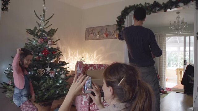 Mother taking a photo of young daughter by Christmas tree