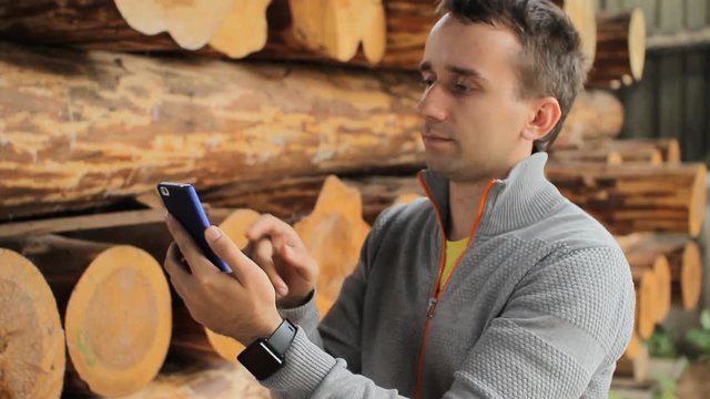 Young man forestry engineer touch phone in front of wood