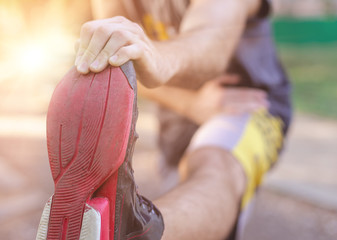 Training outdoors. Young man stretching his legs to warm up. Front angle view.