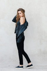 Happy young beautiful woman in black leather jacket black jeans slip-on posing for model tests against textured wall