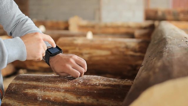 Young man forestry engineer touch smart watch in front of wood