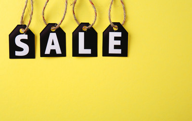 Black paper tags with strings on yellow background. Sale concept