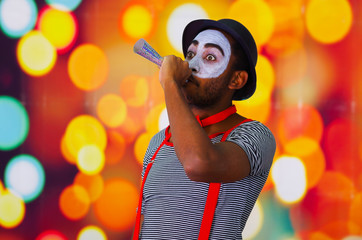 Headshot pantomime man with facial paint posing for camera using blow horn, blurry lights background