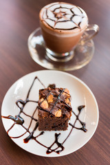 Brownies with chocolate sauce topping on white plate and cocoa.