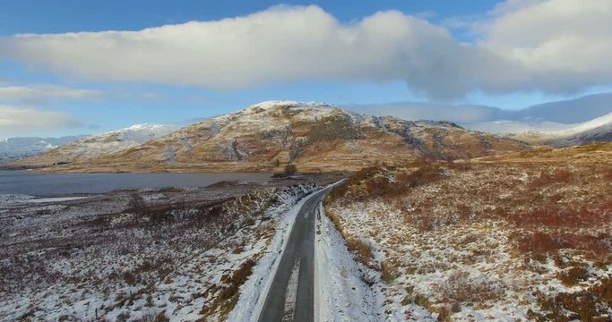 Aerial: Stunning view of road close to lake in Highlands in winter, North Scotland