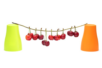 Натюрморт с ягодами черешни и двумя цветными стаканчиками на белом фоне
