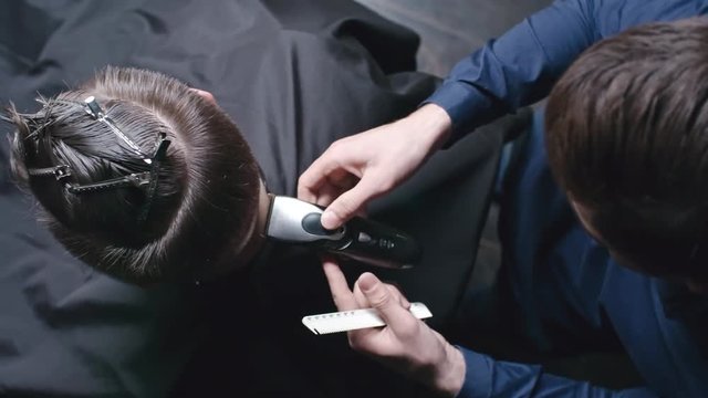 Directly above view of professional barber cutting hair along the neckline of his client with trimmer