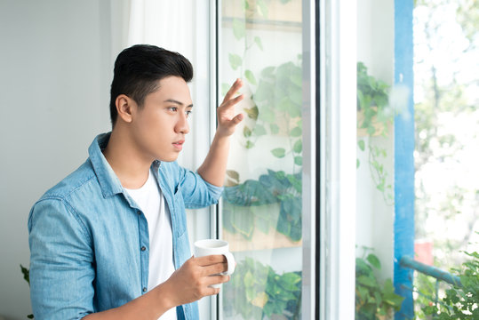 Thoughtful Asian Man Looking Out The Window In Bedroom At Home