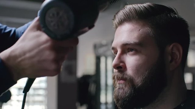 Male hairstylist using hair dryer to style hair of his client