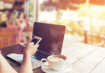 Side view of beautiful young hipster woman's hands busy using her smart phone sitting at wooden table in a coffee shop - retro filter effect and vintage color style
