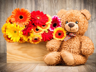 Flowers and a teddy bear on wooden background