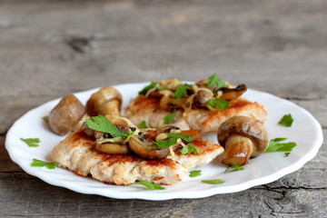 Roasted Turkey fillet with cheese and mushrooms on a plate and on old wooden background. Delicious Turkey cutlets recipe. Closeup