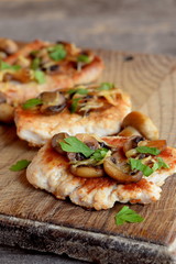 Slices of roasted Turkey meat. Fried Turkey steaks with cheese and mushrooms on a chopping board and an old wooden table. Delicious and easy meat recipe. Closeup