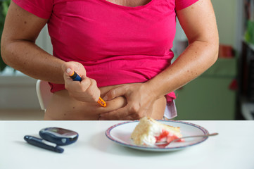 Obraz na płótnie Canvas Female diabetic patient injecting herself with shot of insulin before having a piece of cake for desert.
