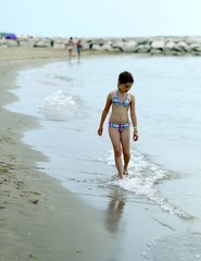 thoughtful little girl in swimsuit on the shore of the sea