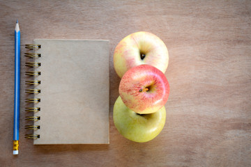 Notebook, pencil, apple on a wooden floor.