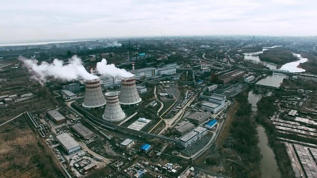 Aerial view of power station with cooling towers producing steam surrounded by large industrial area with factories