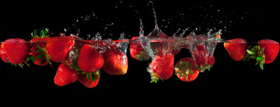 Fototapeta Strawberries splashing into water on a black background