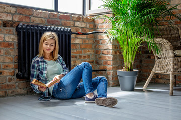 Obraz na płótnie Canvas Blond female sitting on the floor and reading a book.