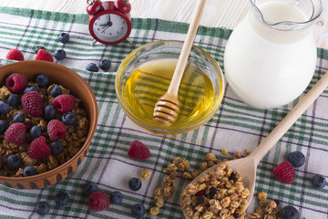 Muesli with fresh berries, honey, milk and alarm clock.