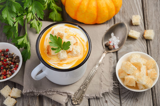 Pumpkin soup with cream and parsley in a mug on wooden background, top view