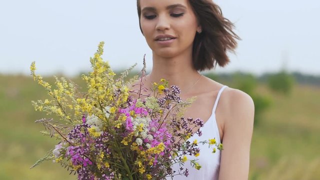 One young woman standing on green field with flower bunch