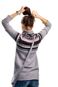 Young Woman Touches Hair. Back View Of Patterned Sweater. Model Is Tying Pony Tail. Example Of Simple Hairdo.