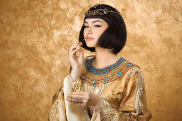 Beautiful Egyptian woman like Cleopatra with perfume bottle on golden background